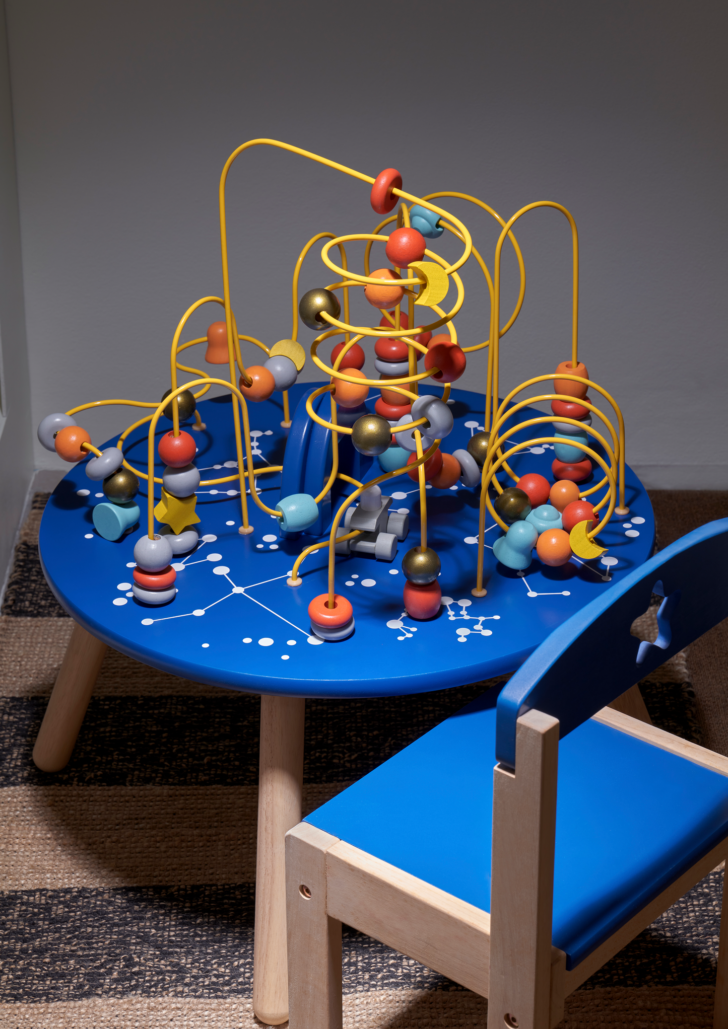 A rectangular wooden activity table with red, green, and blue edges, accompanied by two chairs with one seat in blue and one in yellow.