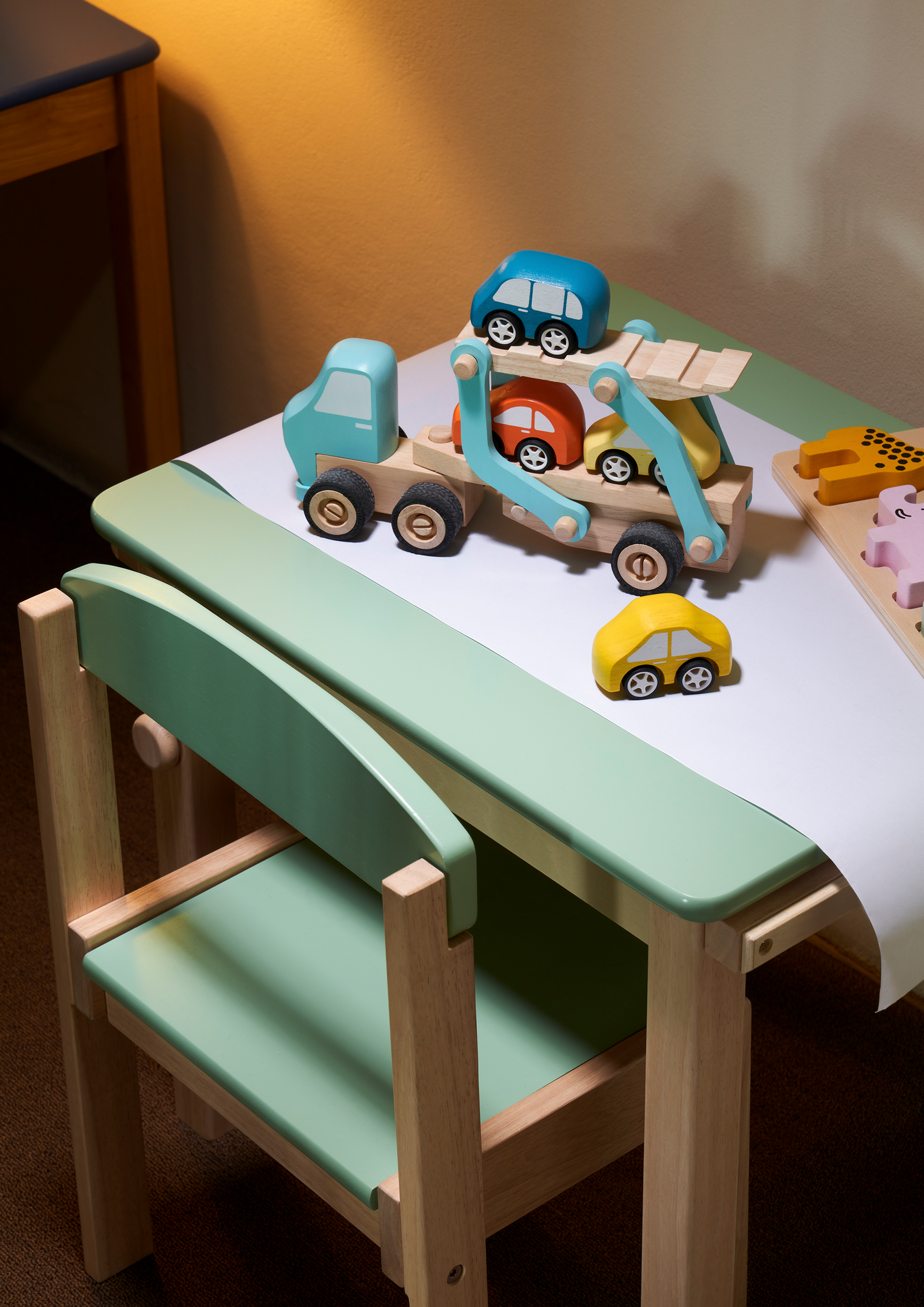 A small wooden desk with a green paper roll holder and cutter, and a matching wooden chair with a green seat cushion.