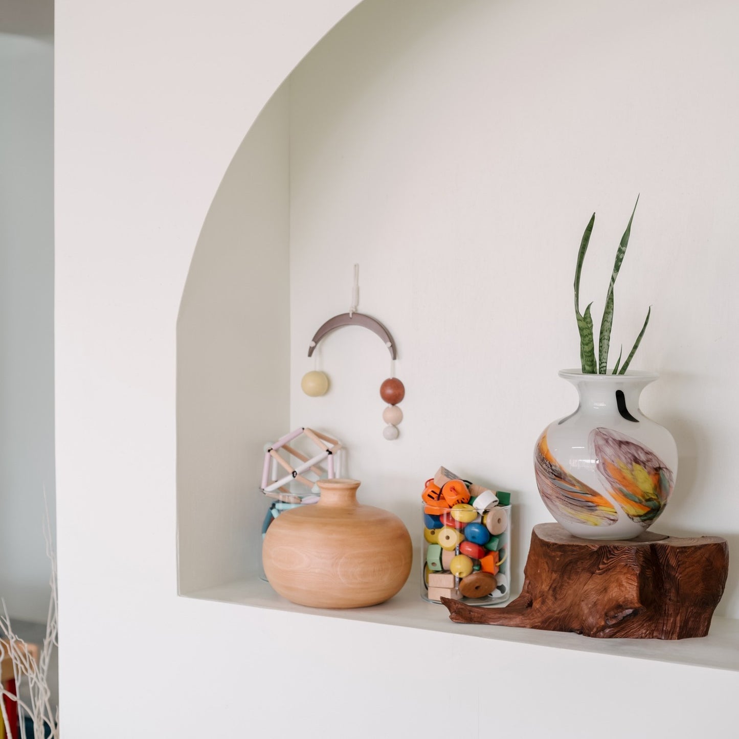 A baby mobile with a wooden arc, attached with colorful geometric shaped hanging elements in brown, beige, black, and white.