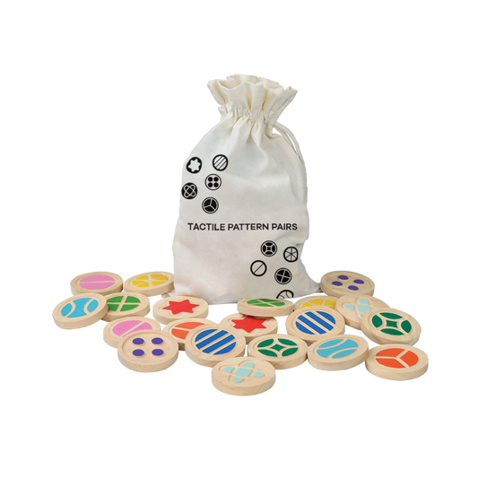 A set of colorful wooden disks with different tactile patterns, placed on a surface near a drawstring canvas bag labeled 'TACHY PATTERN PAIRS'.