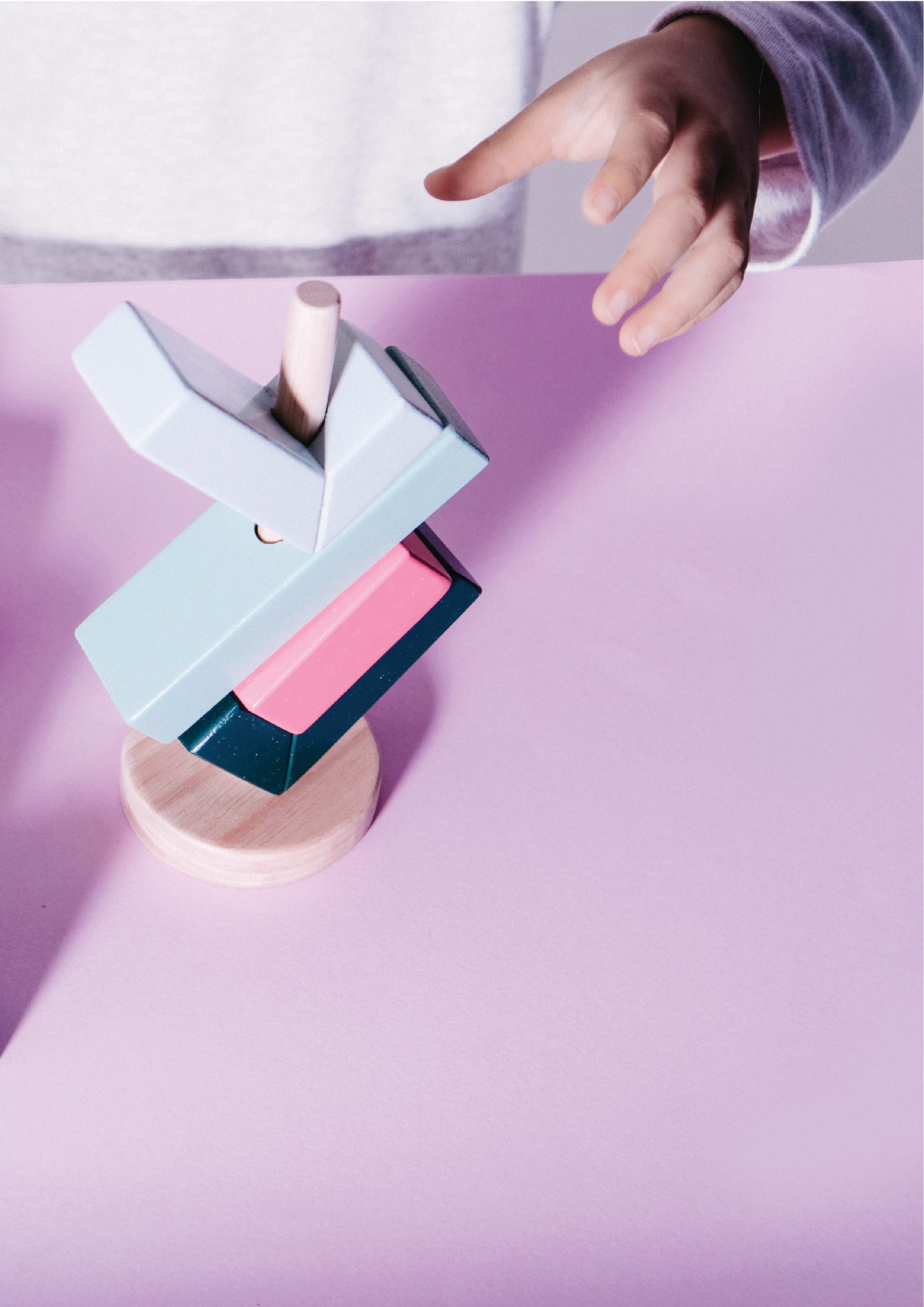 A colorful balance toy consisting of stacked rectangular blocks in shades of green, pink, and blue, arranged in an infinity shape on a wooden rod.