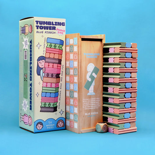 The image shows a wooden tumbling tower game with various colored wooden blocks and a wooden box packaging. A dice is also visible to the side.