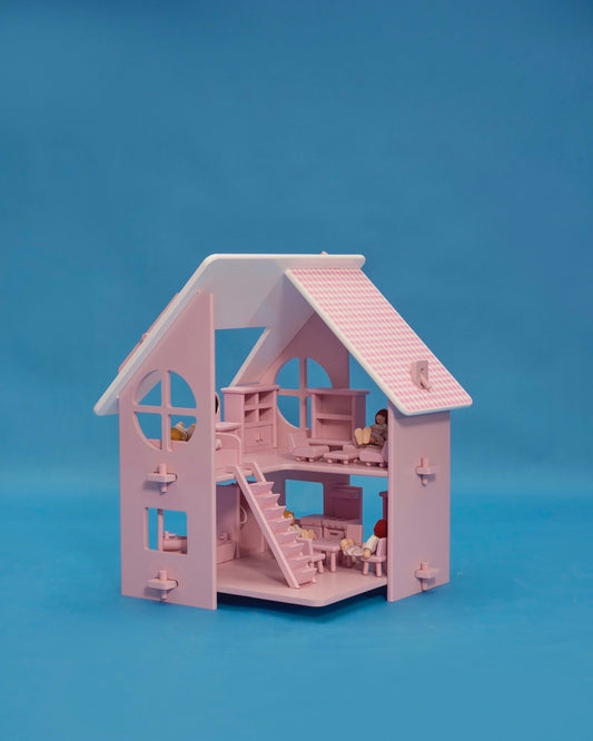 A pink dollhouse with a roof, windows, and a set of stairs. It features a family of five dolls in front, dressed in white with pink accents.