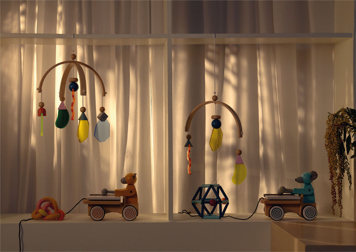 A wooden baby mobile featuring curved wooden arms and colorful hanging shapes in various forms and textures. Designed to engage visual tracking and stimulate sensory development for infants.