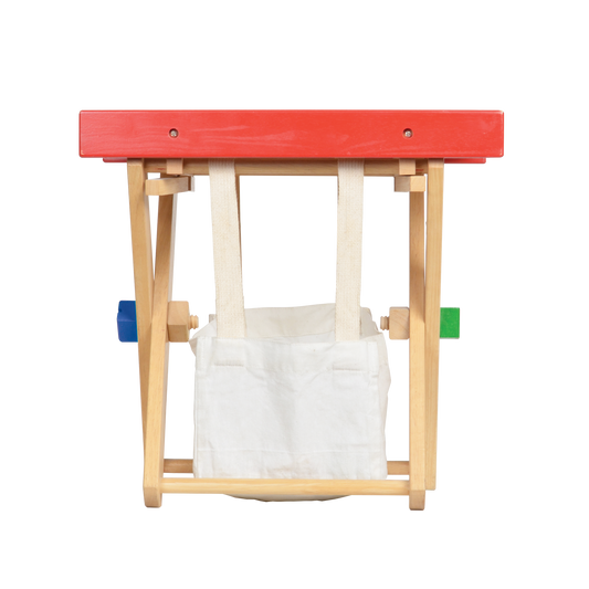 Collapsible wooden work bench for children with a red top and a storage bag underneath.