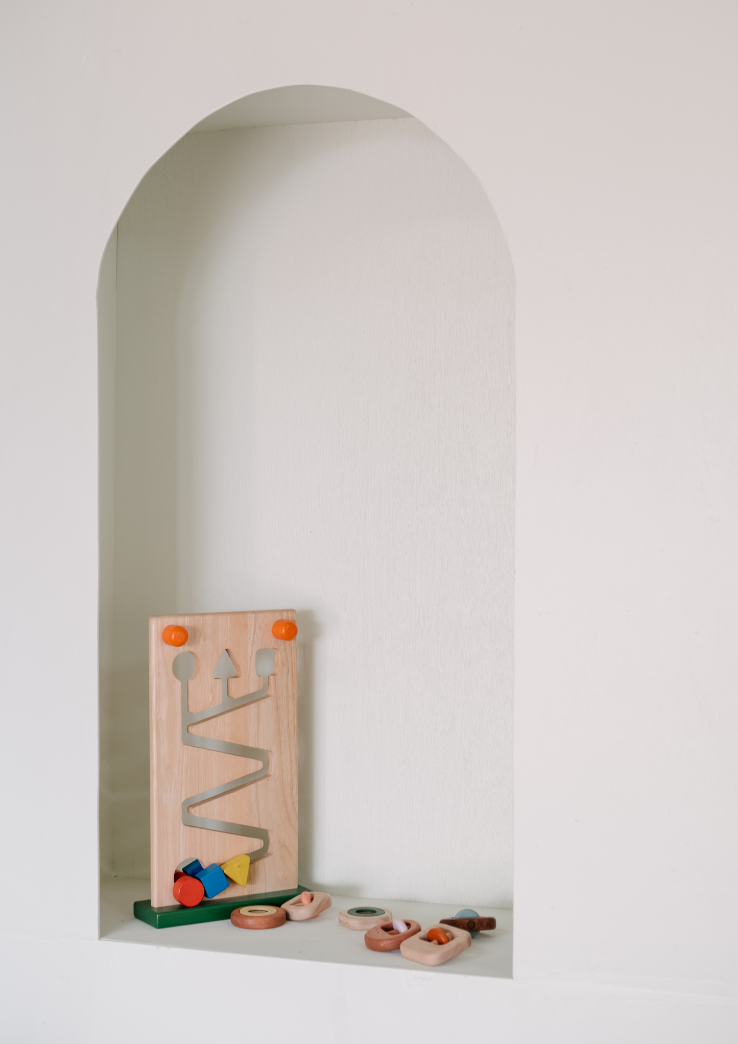 A wooden toy with geometric shapes on the top and a pathway cut out in the center, with colorful wheels at the bottom.