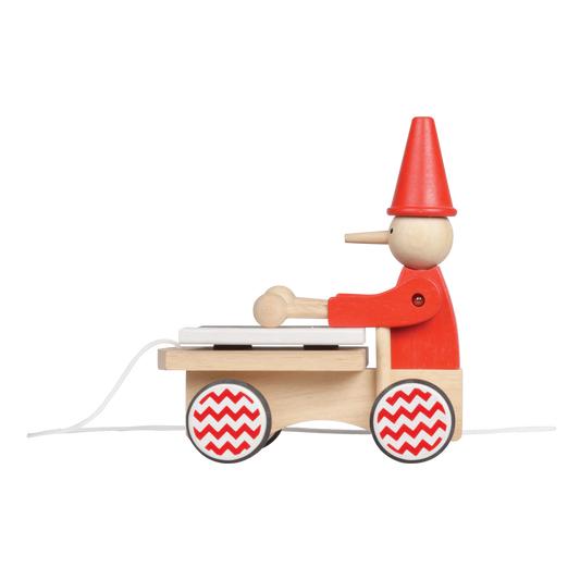 A wooden pull-along toy featuring a character resembling Pinocchio with a red hat, red jacket, attached to a small wooden xylophone on wheels with a red and white zig-zag pattern.
