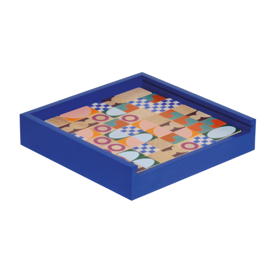A set of multicolored geometric pattern dominoes pieces arranged in a line on a blue tray, with a wooden case in the background.