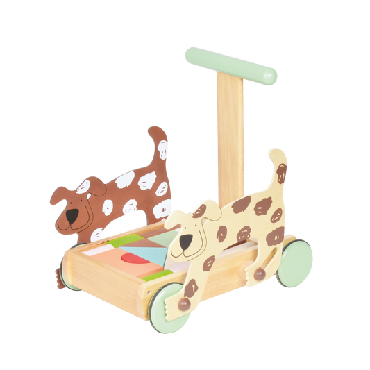 A wooden push toy designed for toddlers, featuring two cartoon-style dogs with spots on each side of the base. The toy has a handle for pushing, four wheels in pastel green, and a colorful geometric pattern on the base. The dogs are smiling, adding a playful and friendly touch.