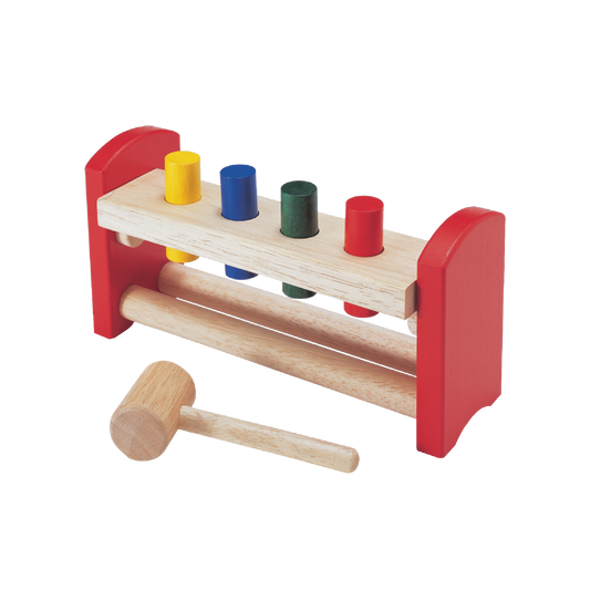 A wooden toy bench with colorful pegs in holes and a wooden mallet, primarily red and natural wood color.