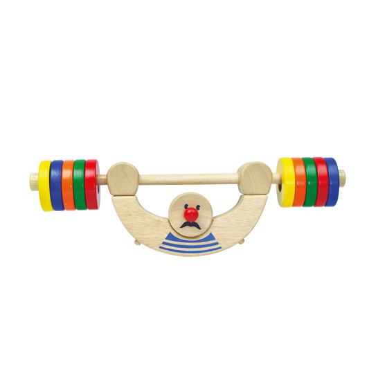 A colorful wooden balance man toy with red, orange, yellow, green, blue, and purple weight plates on a wooden board with a central character illustration.