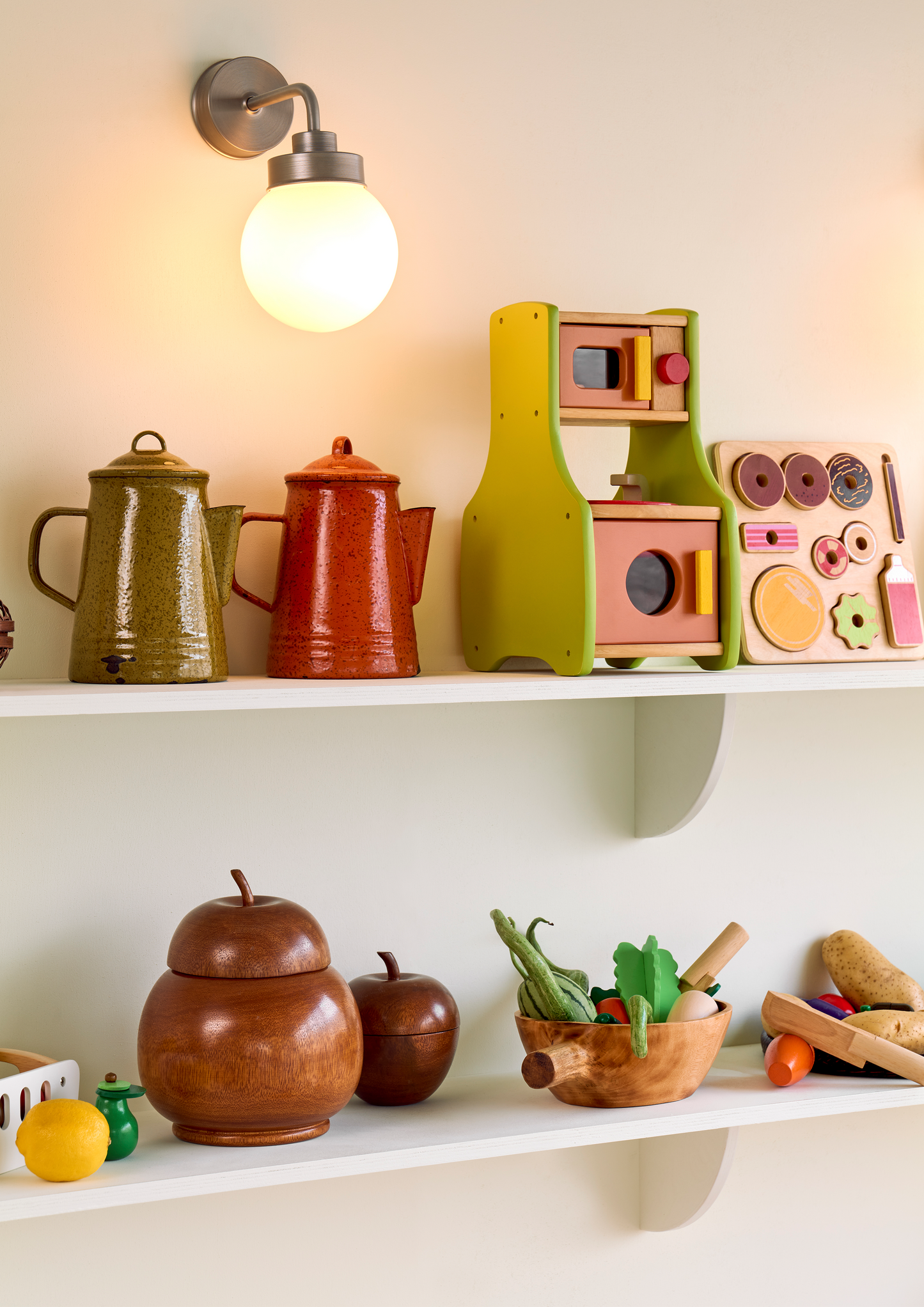 A set of plastic toy fruits including a yellow apple, red apple, green pear, orange, and two tomatoes, accompanied by a white cutting board and a toy knife.
